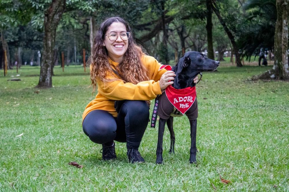 Una mujer sonriente arrodillada junto a un perro con un pañuelo de “adóptame”