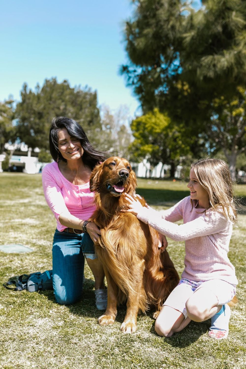 Una madre y su hija acarician a un perro dorado en un parque